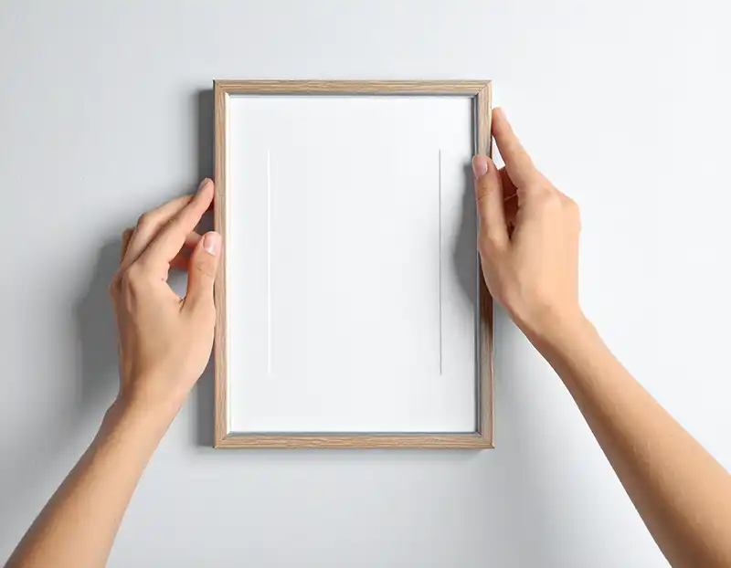 Manos colgando un cuadro en la pared con sistema adhesivo