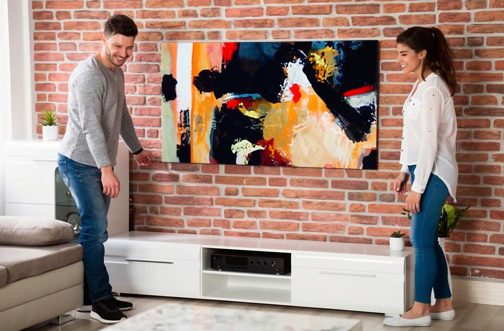 Couple installant un tableau abstrait coloré au-dessus d'un meuble TV dans leur salon moderne