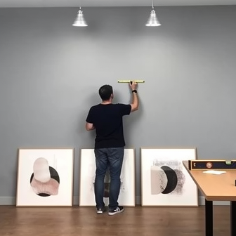 Persona midiendo la pared para colgar cuatro cuadros abstractos con marco